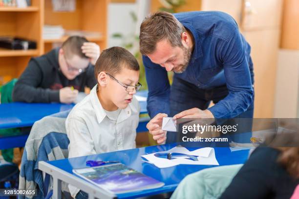 special education teacher holding a model made by intellectually challenged elementary student, looking satisfied with his accomplishment - special education stock pictures, royalty-free photos & images