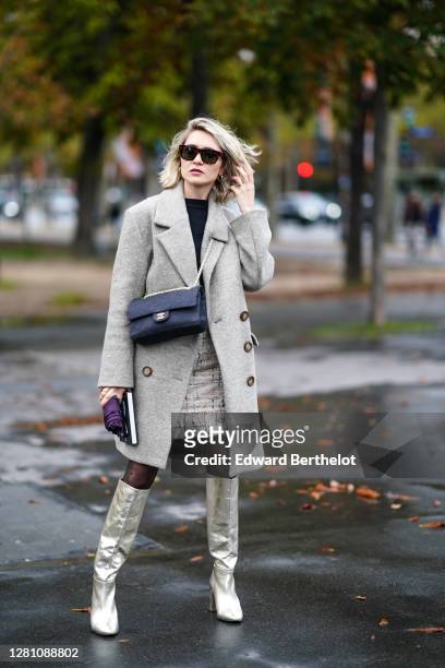 Guest wears sunglasses, a gray wool long coat, a Chanel bag, silver long pointy shiny boots, tights, a white tweed skirt, a black top, earrings,...