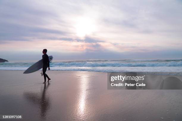 surfer leaving beach at sunset - sennen stock pictures, royalty-free photos & images