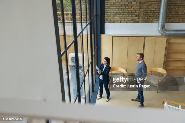female property agent showing man around empty office space - business women looking at new office space stockfoto's en -beelden