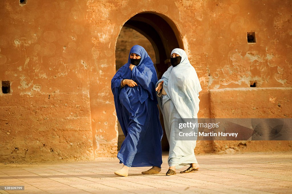 Two Muslim women wearing the traditional chador or nikab (full body cloak) walking past the ramparts that surround the medina in the town of Taroudannt, Morocco. (MR)
