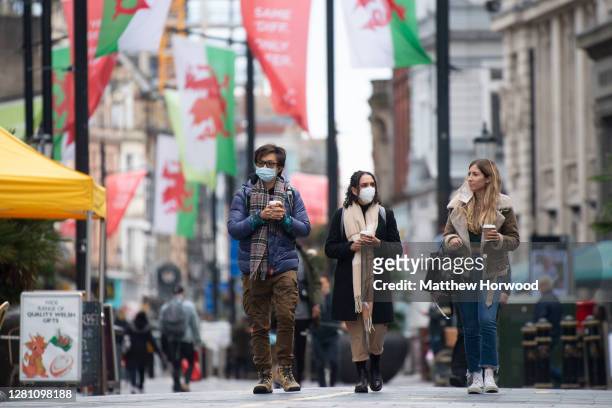 Man and two women wear face masks as they walk up St. Mary Street on October 19, 2020 in Cardiff, Wales. Wales will go into a national lockdown from...