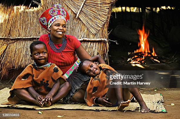 zulu woman in traditional red headdress of a married woman with her children. beehive hut in the background. lesedi cultural village near johannesburg, south africa. - zulu women stockfoto's en -beelden