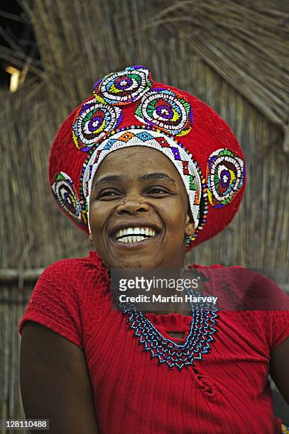zulu woman in traditional red headdress of a married woman. beehive hut in the background. lesedi cultural village near johannesburg, south africa. - zulu women stock pictures, royalty-free photos & images