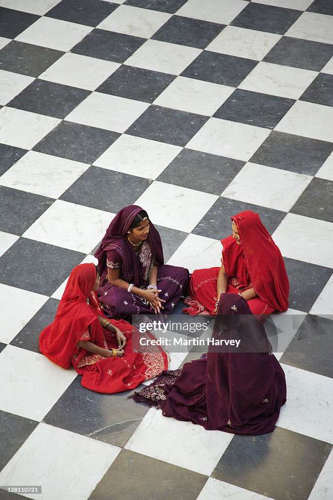 Four Indian women in traditional saris sitting on the chequered floor of the Peacock courtyard at the City Palace Complex. Udaipur, India. (MR) (PR: Property Released)