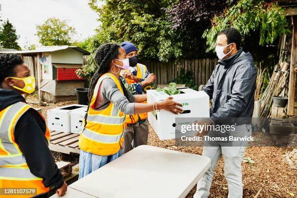 man receiving csa box from volunteer at community garden - assistance sociale photos et images de collection