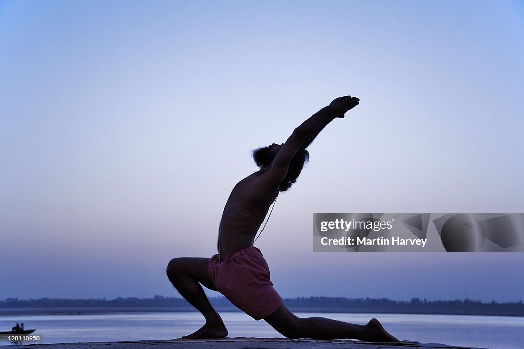 World famous yogi teacher, Dr. Rakesh Yogi, in virbhadrasana yoga posture. Warriors yoga posture. Sunrise over the Ganges River, India. (MR)