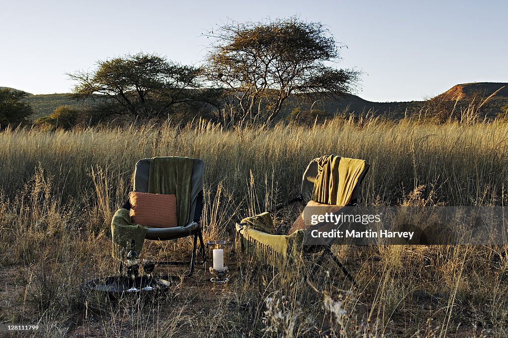 Taking luxurious sunsets and relaxation another step with a glass of wine on a canvas chair amidst the beautiful grassy landscape of Okonjima Private Game Reserve, Namibia. Scenic view of Omboroko Mountains in background. (PR: Property Released)