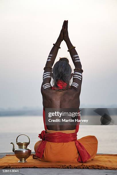 sadhu or holy man performing manas puja. this religious ritual takes place during sunrise. the little brass pot he uses is called a kamandal. buddhist tourists in boat watching ritual. ganges river, varanasi, india. (mr) - hindoeïsme stockfoto's en -beelden