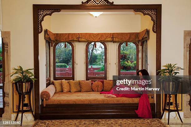 tourist sitting on couch by bay window of a historical suit in taj rambagh palace hotel in jaipur, part of the taj hotel group. india. (mr) - india palace stock pictures, royalty-free photos & images
