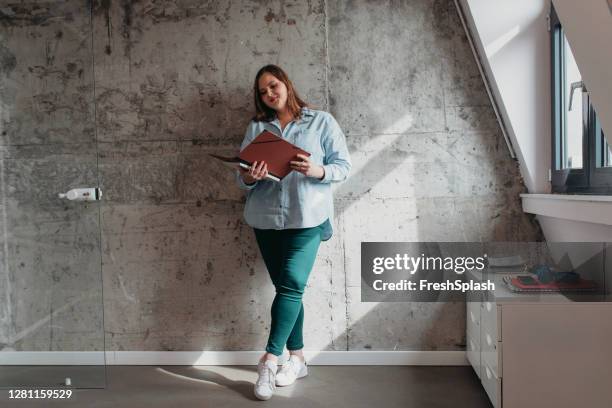 jonge onderneemster die zich in het bureau bevindt en documenten/rapporten leest - blank brochure stockfoto's en -beelden