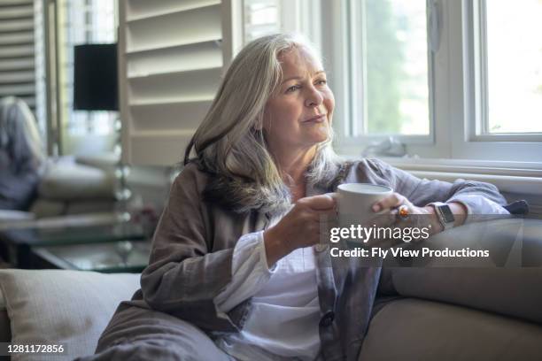 una hermosa mujer mayor mira por una ventana - viuda fotografías e imágenes de stock