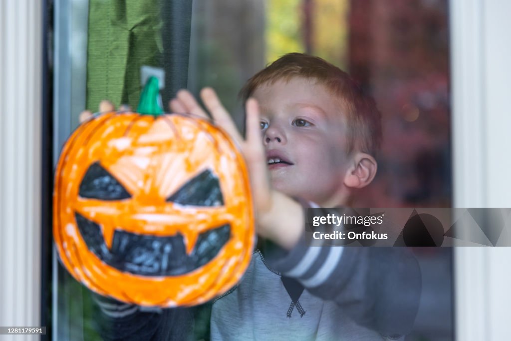 Young Boy sticking his pumpkin drawing on home window