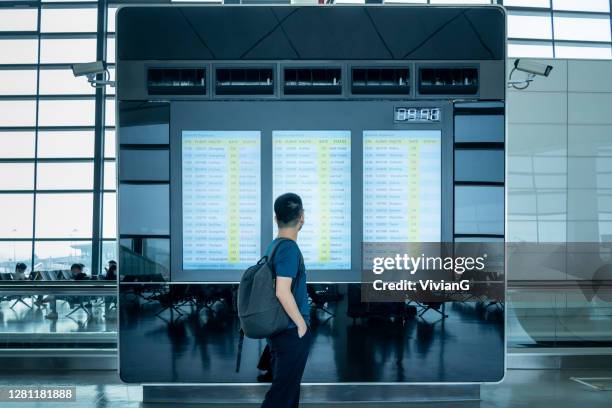 junge männliche reisende beobachten und warten auf flugzeitplan auf boarding-zeit-monitor-bildschirm - digitale beschilderung stock-fotos und bilder
