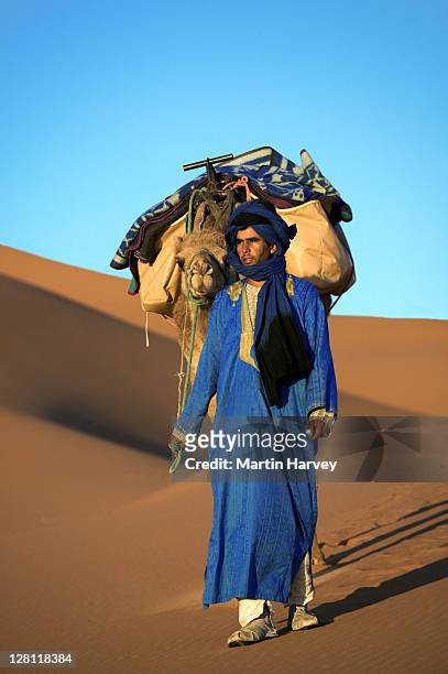 tuareg man dressed in traditional blue robe with camel in the erg chebbi area. sahara desert. morocco - touareg 個照片及圖片檔