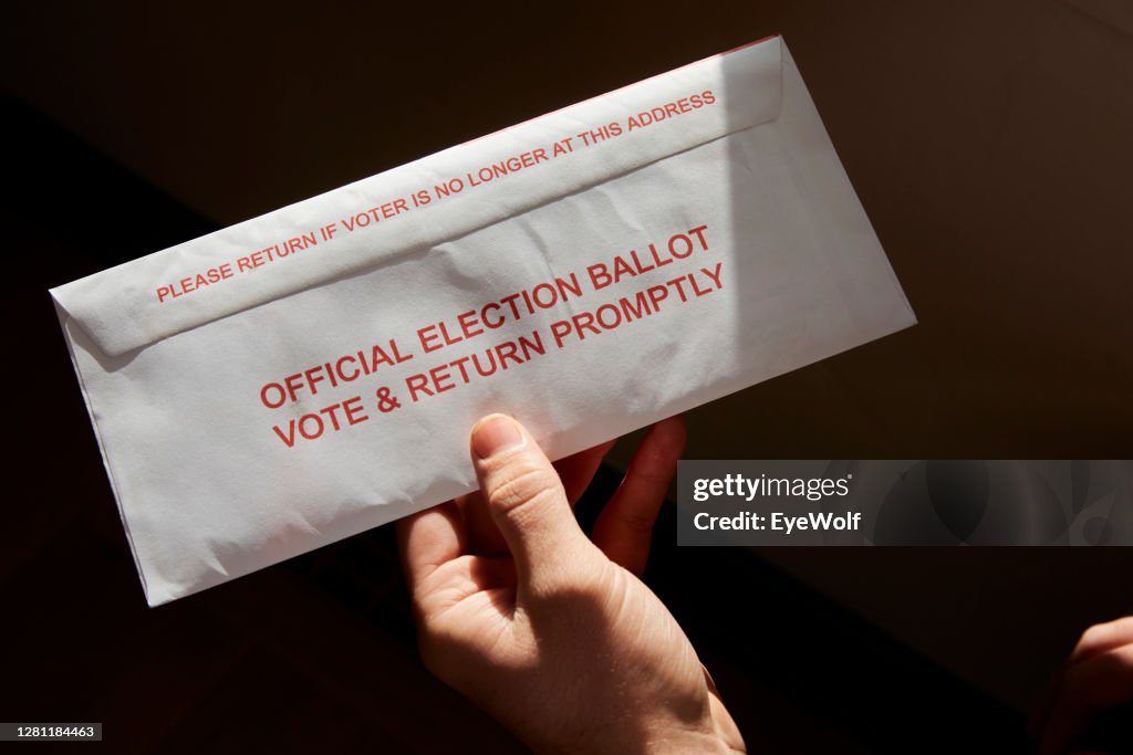 A person standing inside his home holding his mail in voting ballot