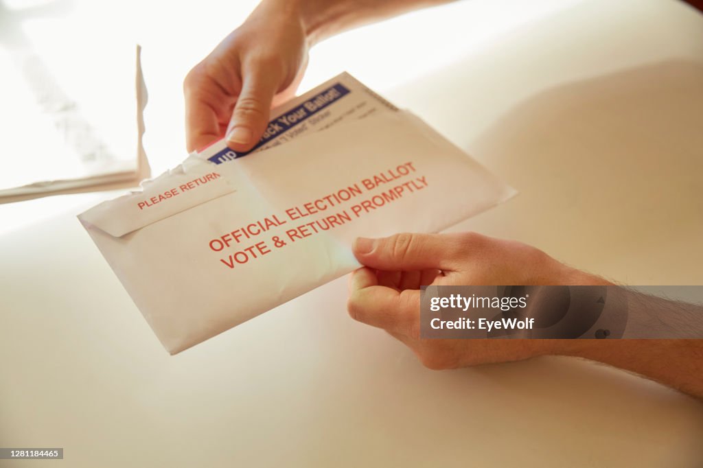 A person inside their home opening up their vote by mail ballot envelope.