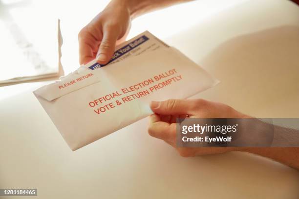 a person inside their home opening up their vote by mail ballot envelope. - voting by mail stockfoto's en -beelden