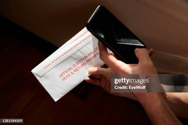 a person taking a photo of their election ballot envelop inside their home, with a rainbow streaming across it. - postit photos et images de collection