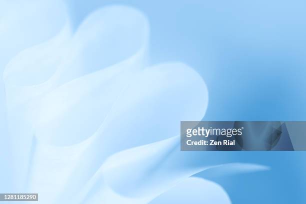 abstract image of white paper with edges forming curves against blue blurry background - light blue paper stock pictures, royalty-free photos & images