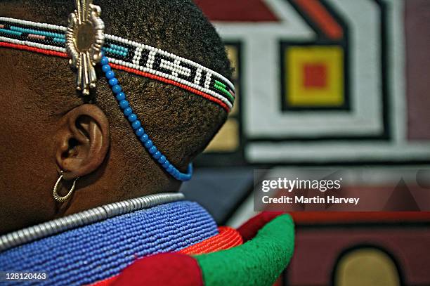 ndebele woman dressed in traditional costume of a married woman. traditional geometric wall paintings of ndebele village in the background. lesedi cultural village near johannesburg, south africa - johannesburg stockfoto's en -beelden