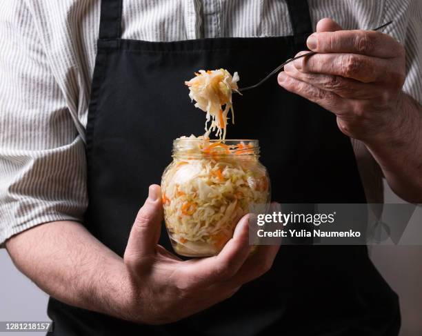 a man in an apron holding a fermented cabbage. - pickle jar stockfoto's en -beelden