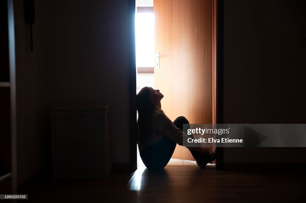 Backlit teenager sitting in a dark indoor doorway in contemplation