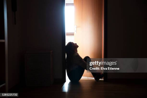 backlit teenager sitting in a dark indoor doorway in contemplation - one teenage girl only ストックフォトと画像