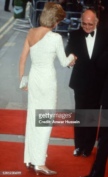 Diana, Princess of Wales, wearing a white, one shoulder evening gown, covered in silver bugle beads and designed by Hachi, arrives for the premiere...