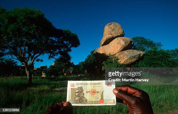 stockillustraties, clipart, cartoons en iconen met man holding currency showing balancing rocks outside harare, zimbabwe - zimbabwe