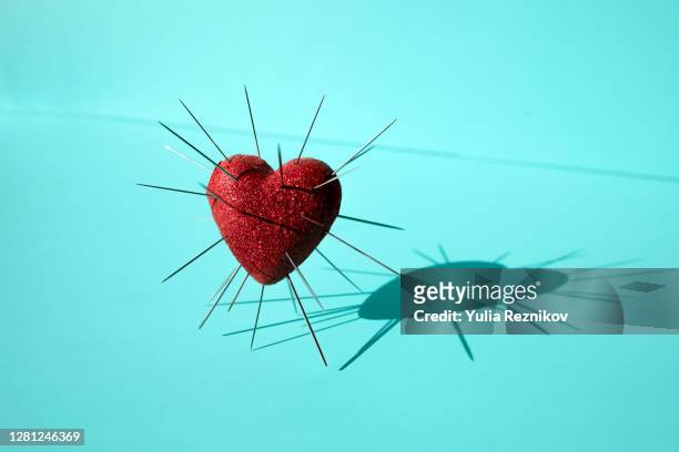shiny red heart shape with needles inserted on the blue background - brustet hjärta bildbanksfoton och bilder