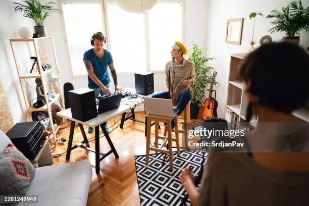 young woman filming two caucasian musicians making music in the music studio - woman in guitar making studio stock pictures, royalty-free photos & images