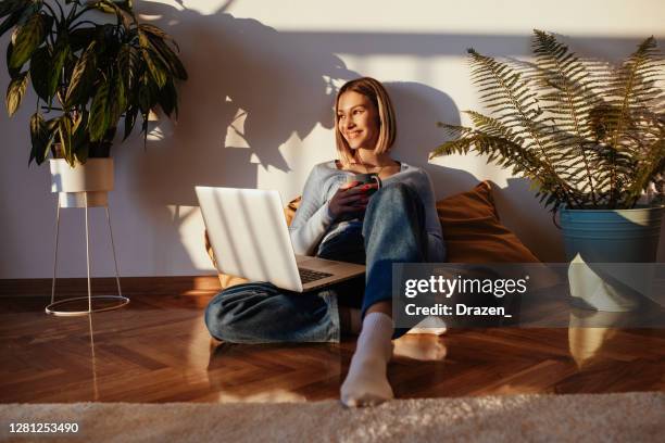 junge frau arbeitet auf laptop zu hause, denken und lächeln - gemütlich stock-fotos und bilder