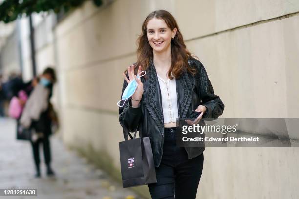 Model wears a black leather jacket, black pants, holds a blue face mask, outside Kenzo, during Paris Fashion Week - Womenswear Spring Summer 2021, on...