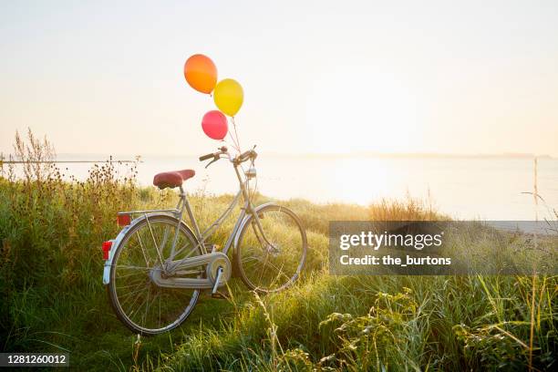 bicycle with colorful balloons by the sea during sunrise - birthday concept stock-fotos und bilder