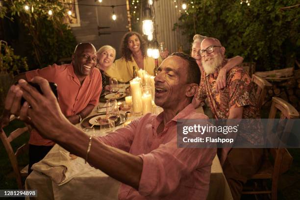 friends taking a self with a phone and dining outside on a warm summers evening. - dinner party with friends stock pictures, royalty-free photos & images