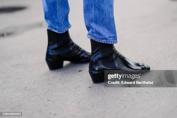 Guest wears blue denim jeans, black leather pointy shiny boots with Chanel logo, outside Chanel, during Paris Fashion Week - Womenswear Spring Summer...