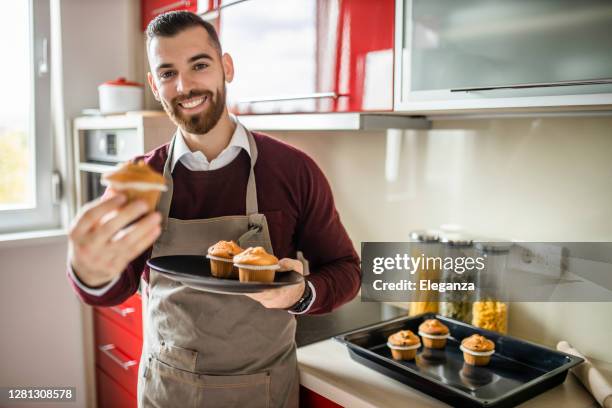 young man wearing apron and preparing muffins in his kitchen - man baking cookies stock pictures, royalty-free photos & images