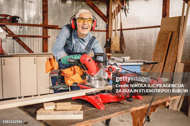 de rijpe vrouwelijke timmerman snijdt een stuk van raad met een mijterzaag. - elektrisch gereedschap stockfoto's en -beelden