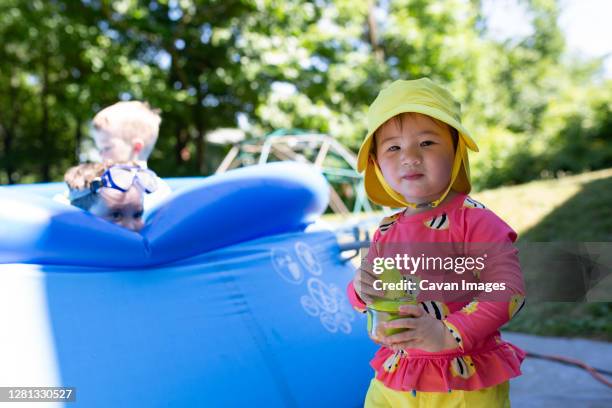 toddler girl wearing yellow sun hat eats snack next to backyard pool - baby sun hat stock-fotos und bilder