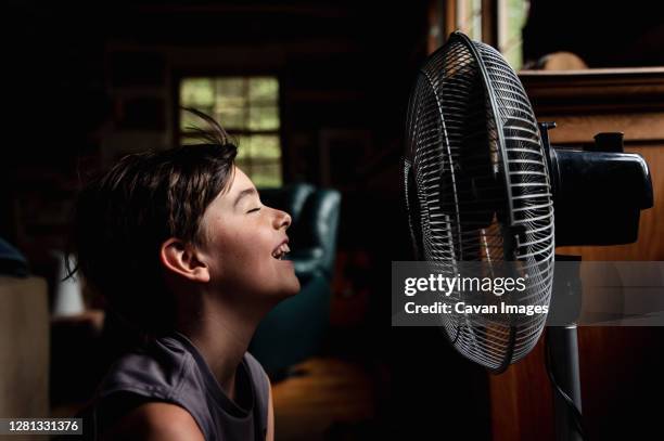 young boy with eyes closed cooling off in front of a fan in dark room. - electric fan stockfoto's en -beelden