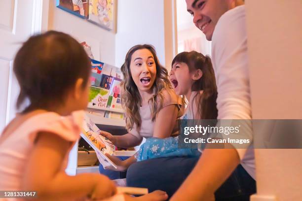 family of four sitting on the floor and reading children's books. - mom smug stock pictures, royalty-free photos & images