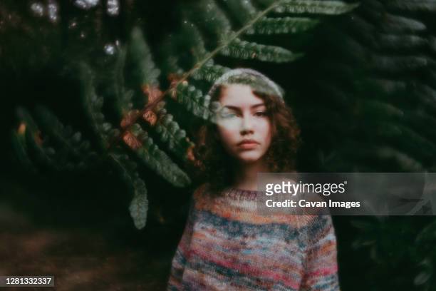girl standing behind leaves in sweater and hat - digital composite stock-fotos und bilder