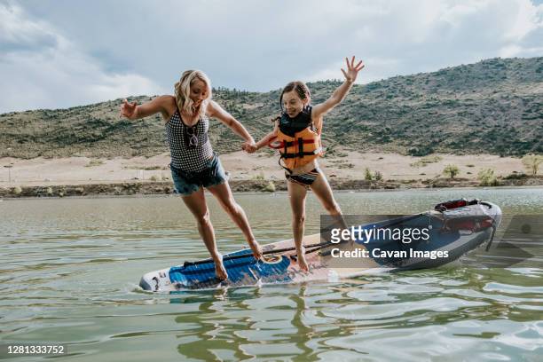 horizontal portrait of mom and daughter jumping off a paddle board - denver summer stock pictures, royalty-free photos & images