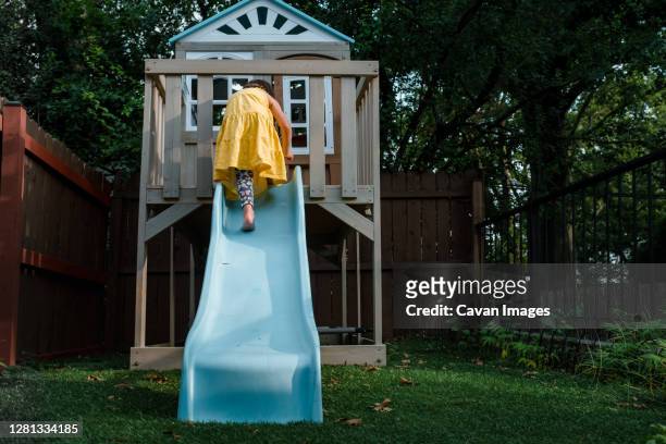 young girl in yellow dress climbing up a blue slide - casa de brinquedo imagens e fotografias de stock