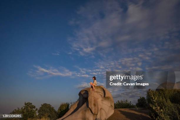 young girl sits on top of a boulder at a playground with blue sky - denver summer stock pictures, royalty-free photos & images