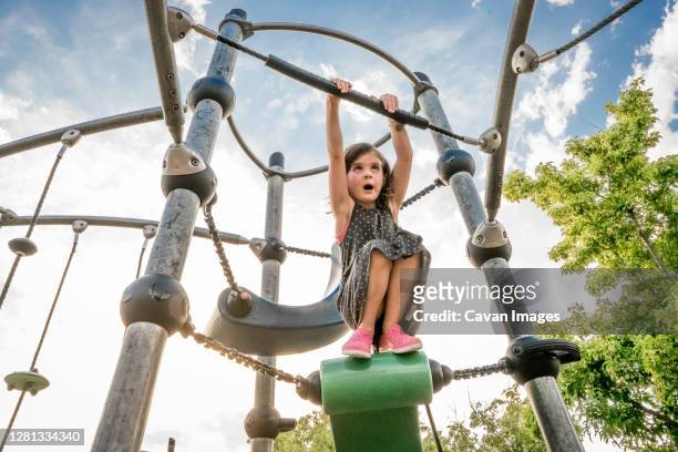 focused young girl anticipates next move on monkey bars at playground - jungle gym stock pictures, royalty-free photos & images