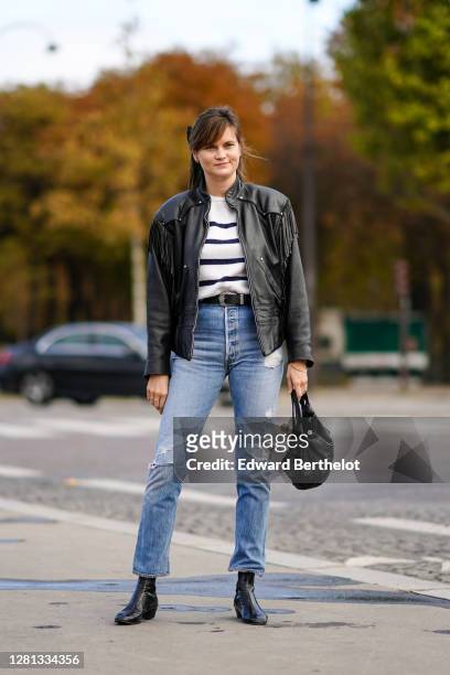 Guest wears a black leather jacket with fringes, a black and white striped pullover, a belt, blue ripped denim jeans pants, a black leather bag,...