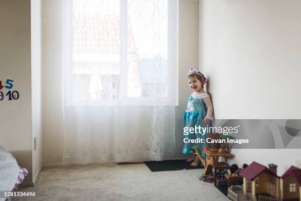 smiling girl in princess costume standing next to toys by window - kanten jurk stockfoto's en -beelden