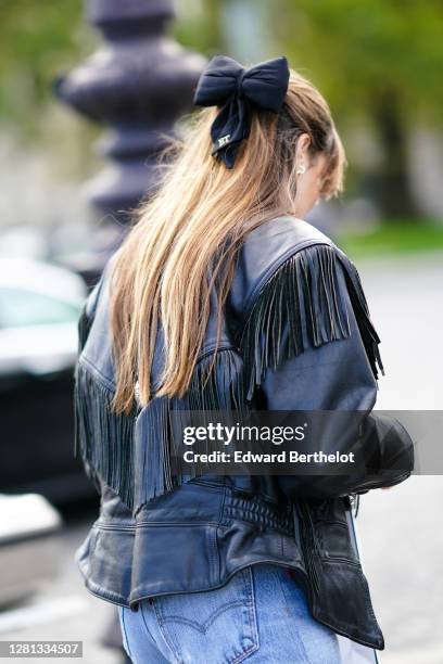 Guest wears a hair bow tie, a black leather jacket with fringes, outside Chanel, during Paris Fashion Week - Womenswear Spring Summer 2021, on...